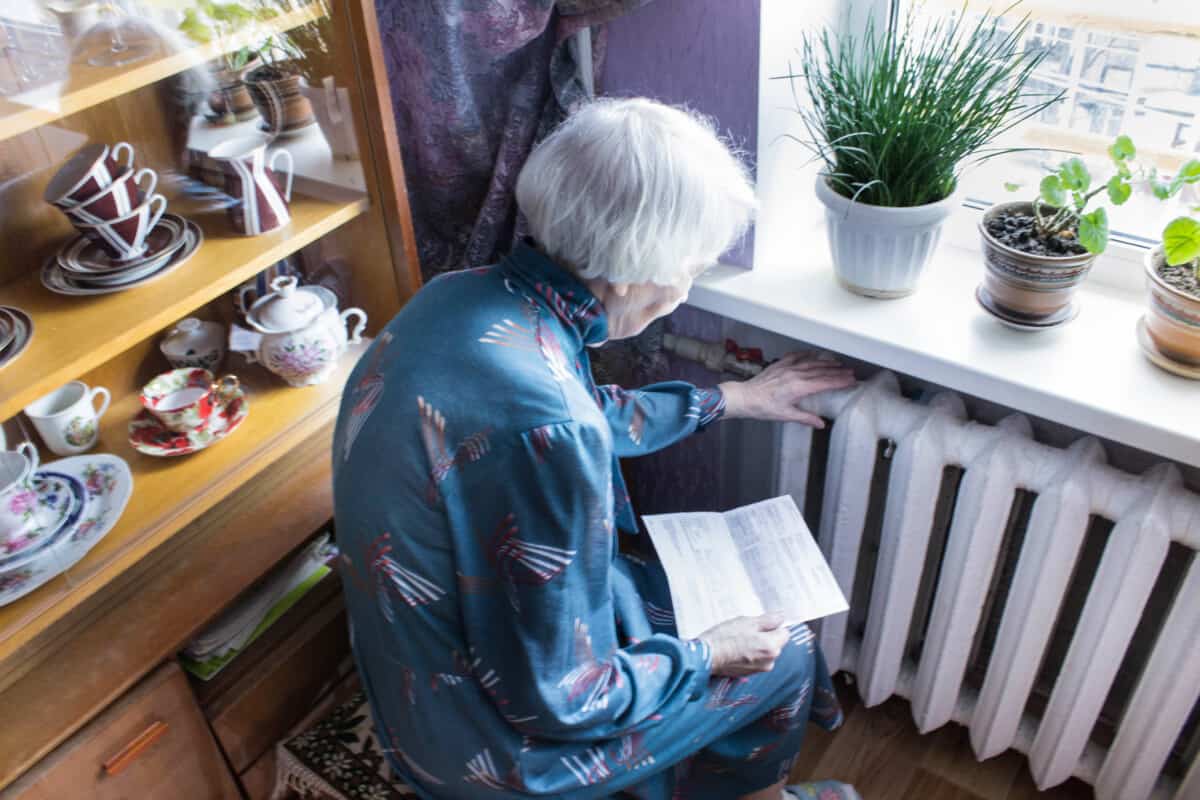 Woman holding sitting by radiator holding her heating bill.