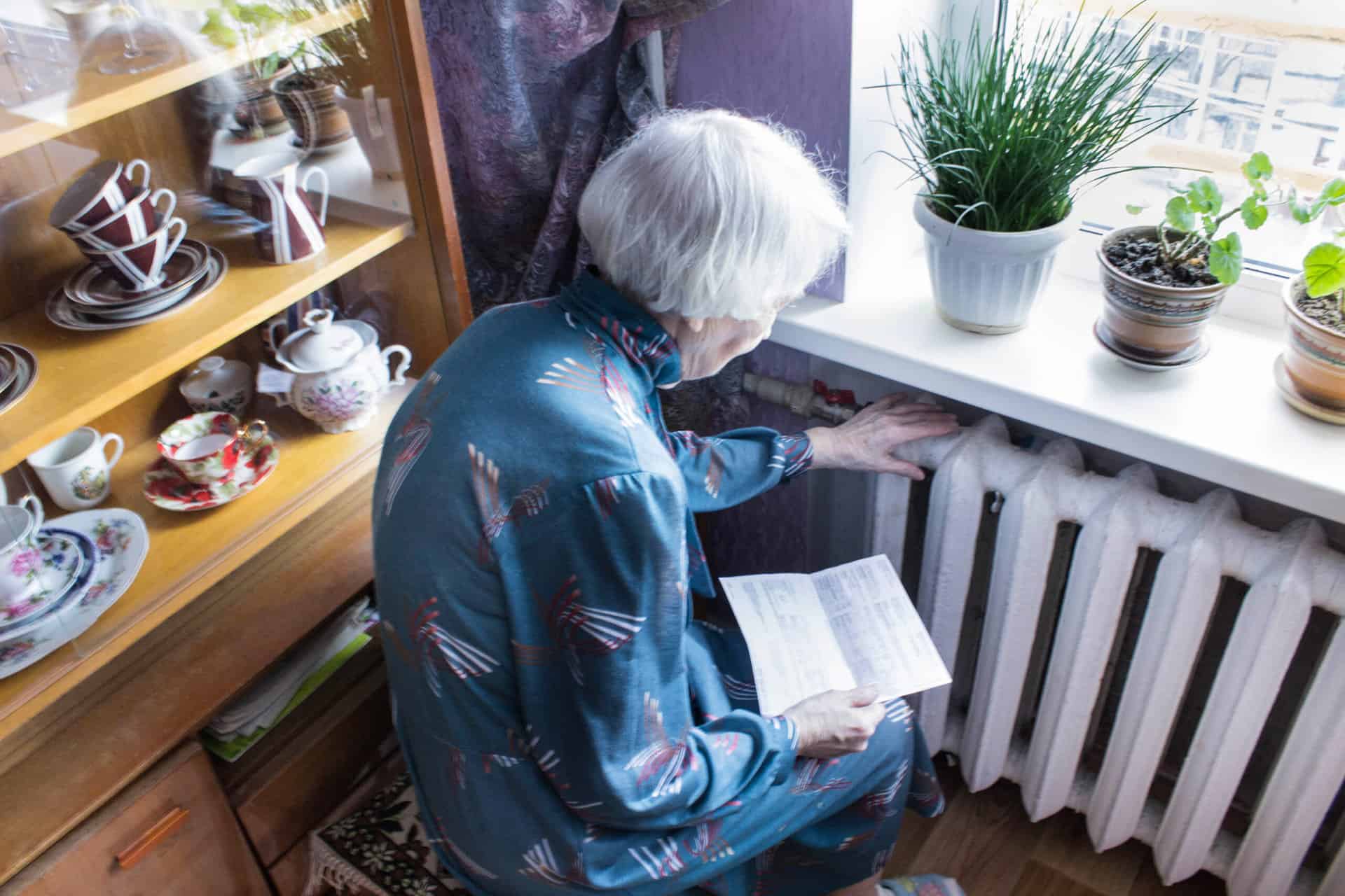 Woman holding sitting by radiator holding her heating bill.