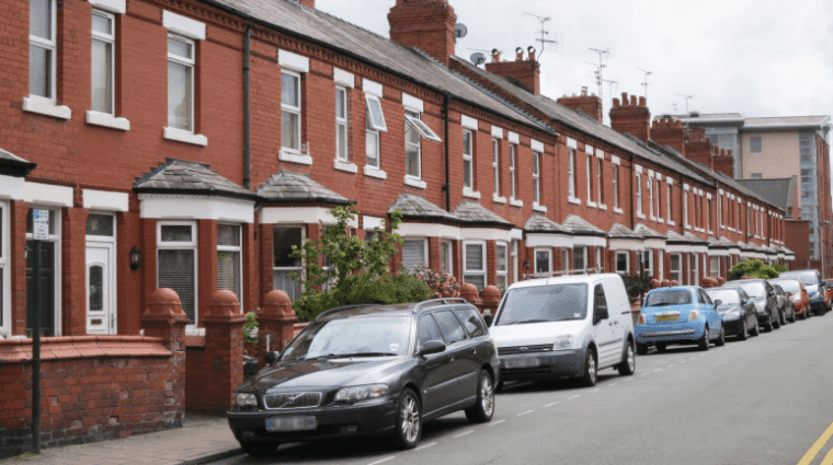 A street of terraced, red brick houses in the UK with cards parallel parked in front