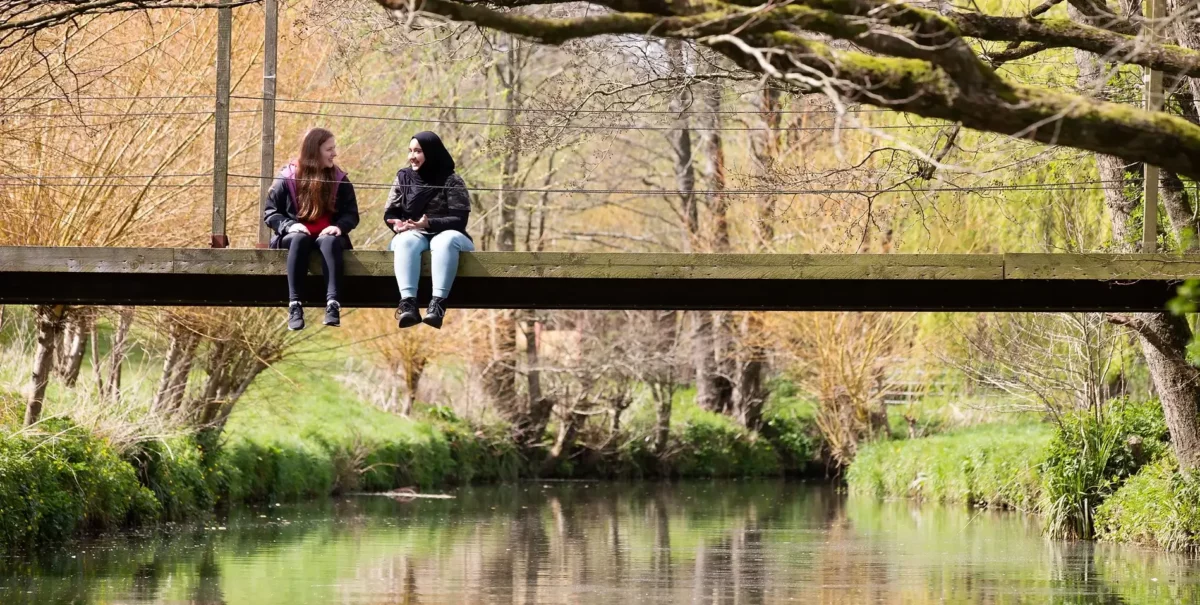 Two teenagers sit on a bridge over a river