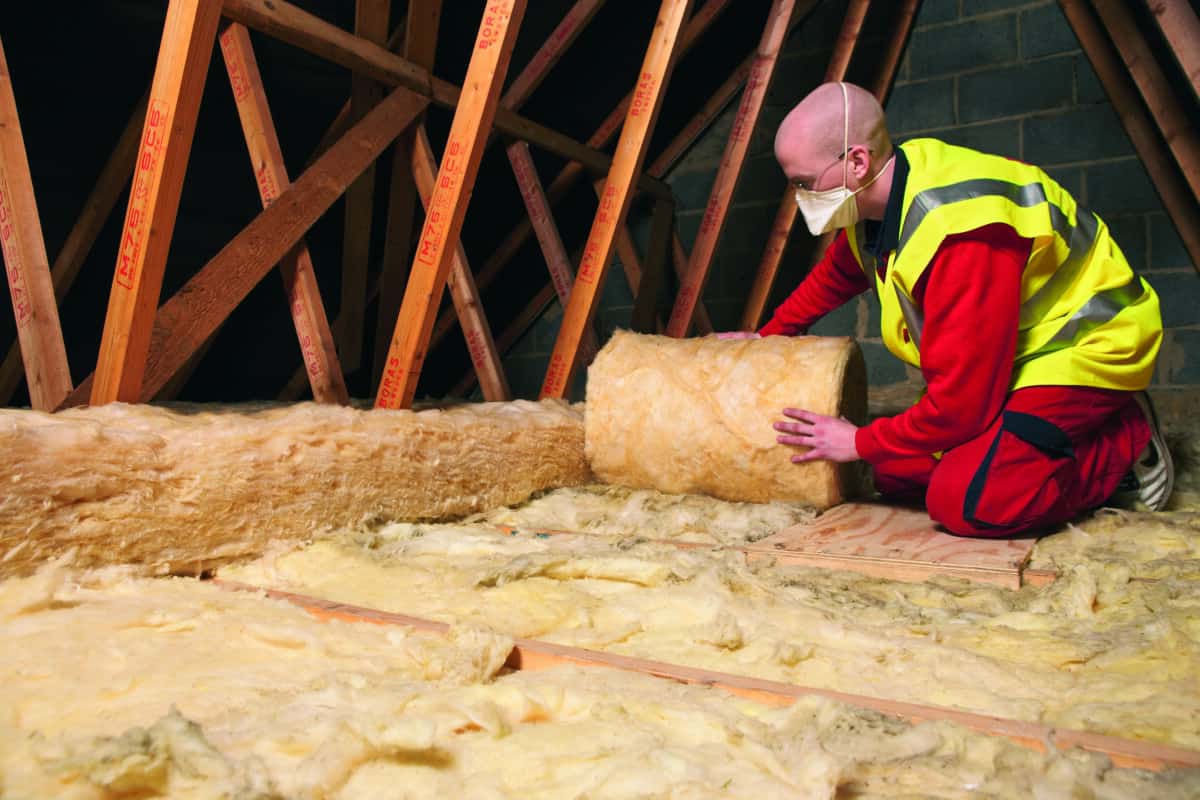 A tradesperson installs loft insulation.