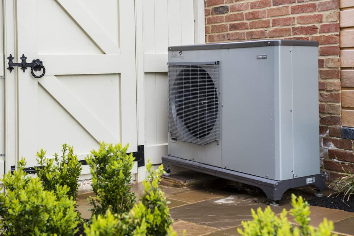 An air source heat pump attached to the side of a house in a garden in England