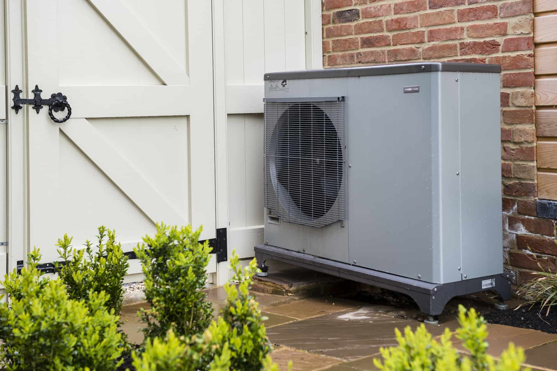 An air source heat pump attached to the side of a house in a garden in England