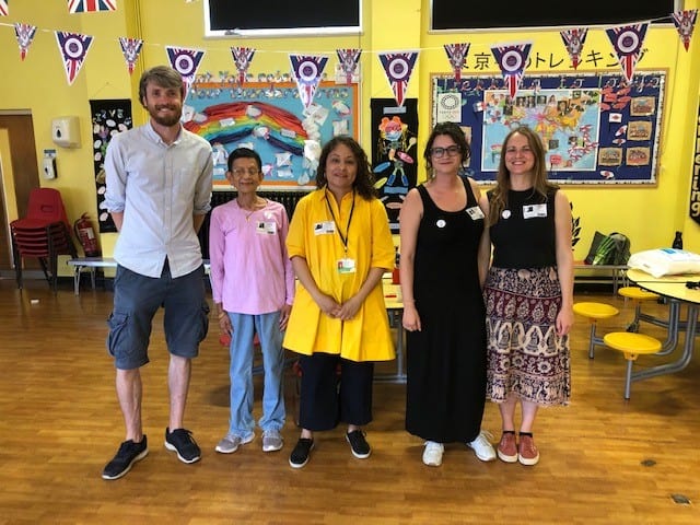 5 teachers and trainers stand smiling at the camera in a colourful classroom
