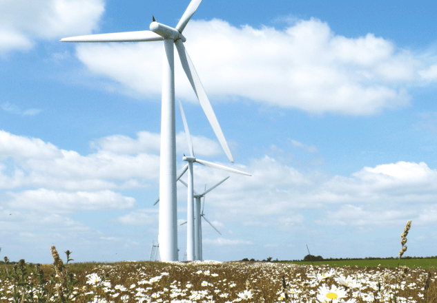 A row of medium-sized wind turbines in a field against a bright blue sky.