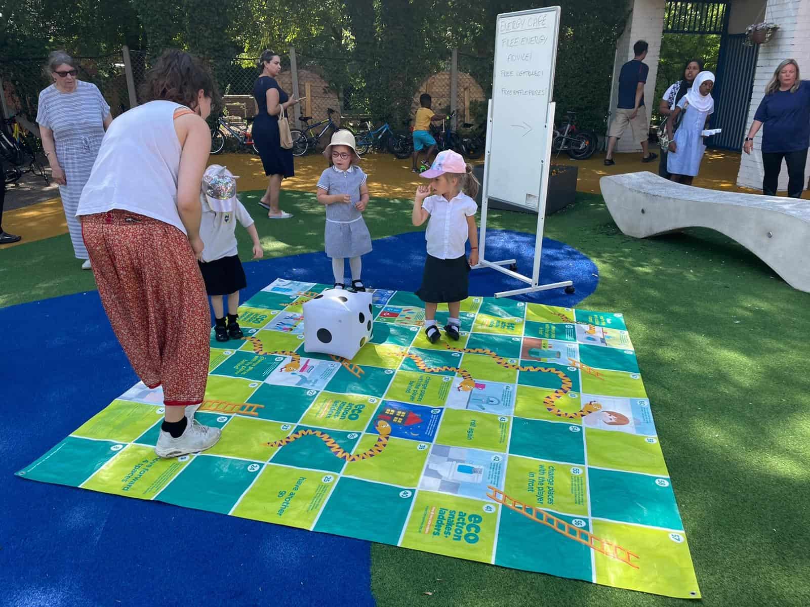 Young children play on a large snakes and ladders board with a large dice