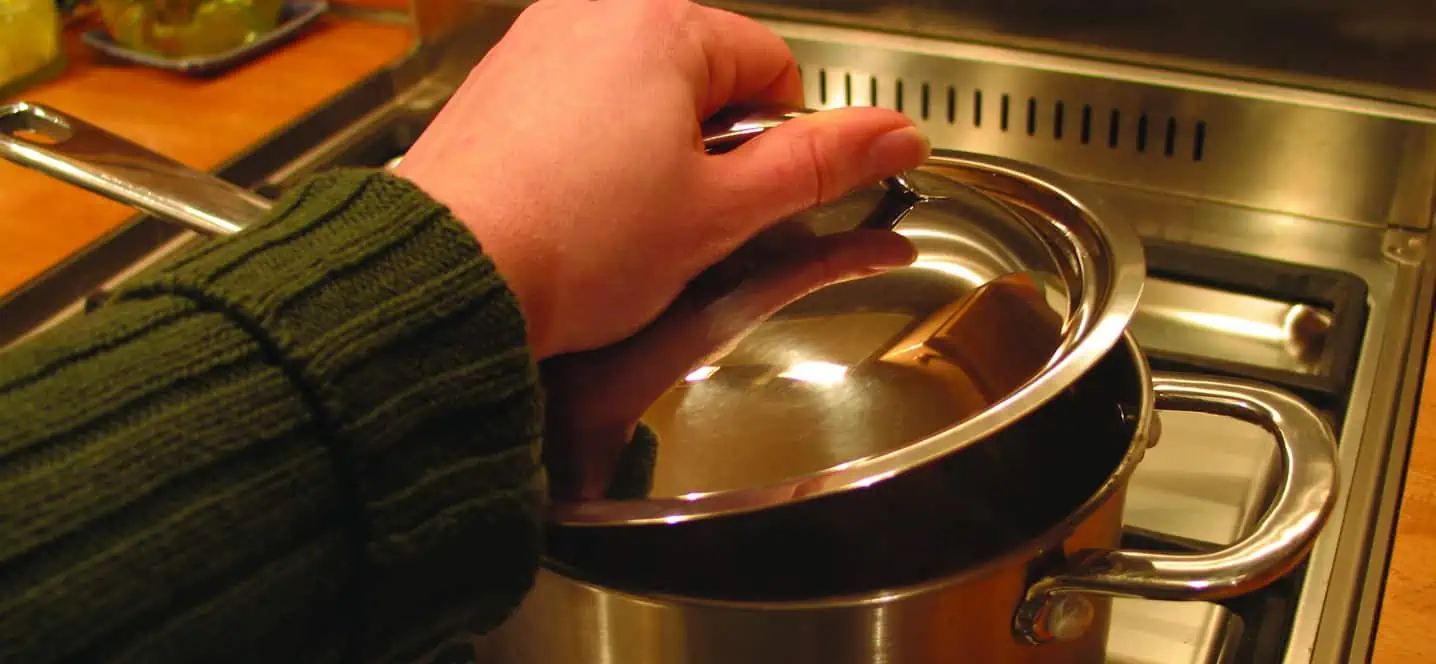 S person in the kitchen replaces the lid on a saucepan to prevent the room becoming too steamy