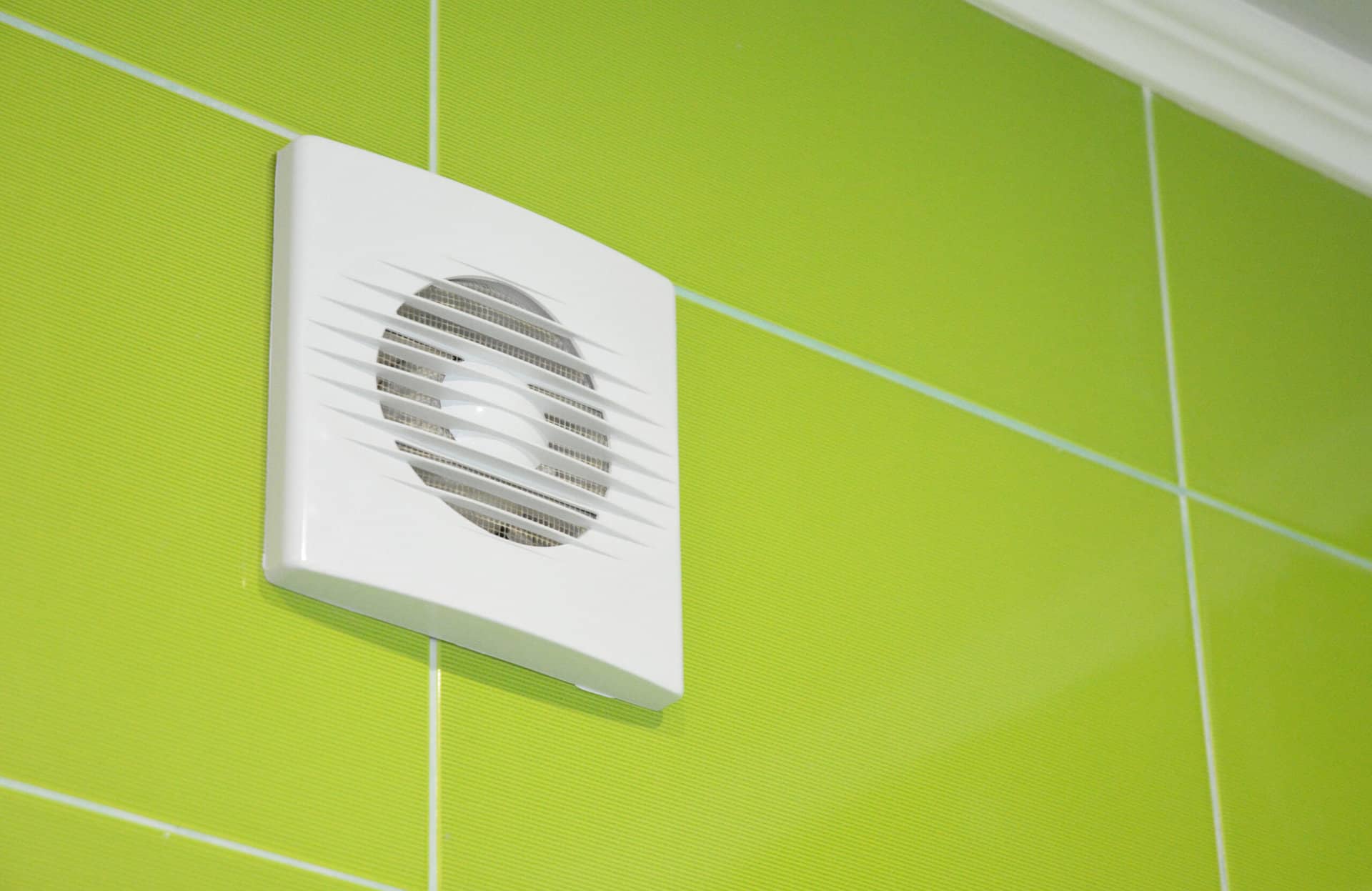 Extractor fan on green tiled bathroom wall
