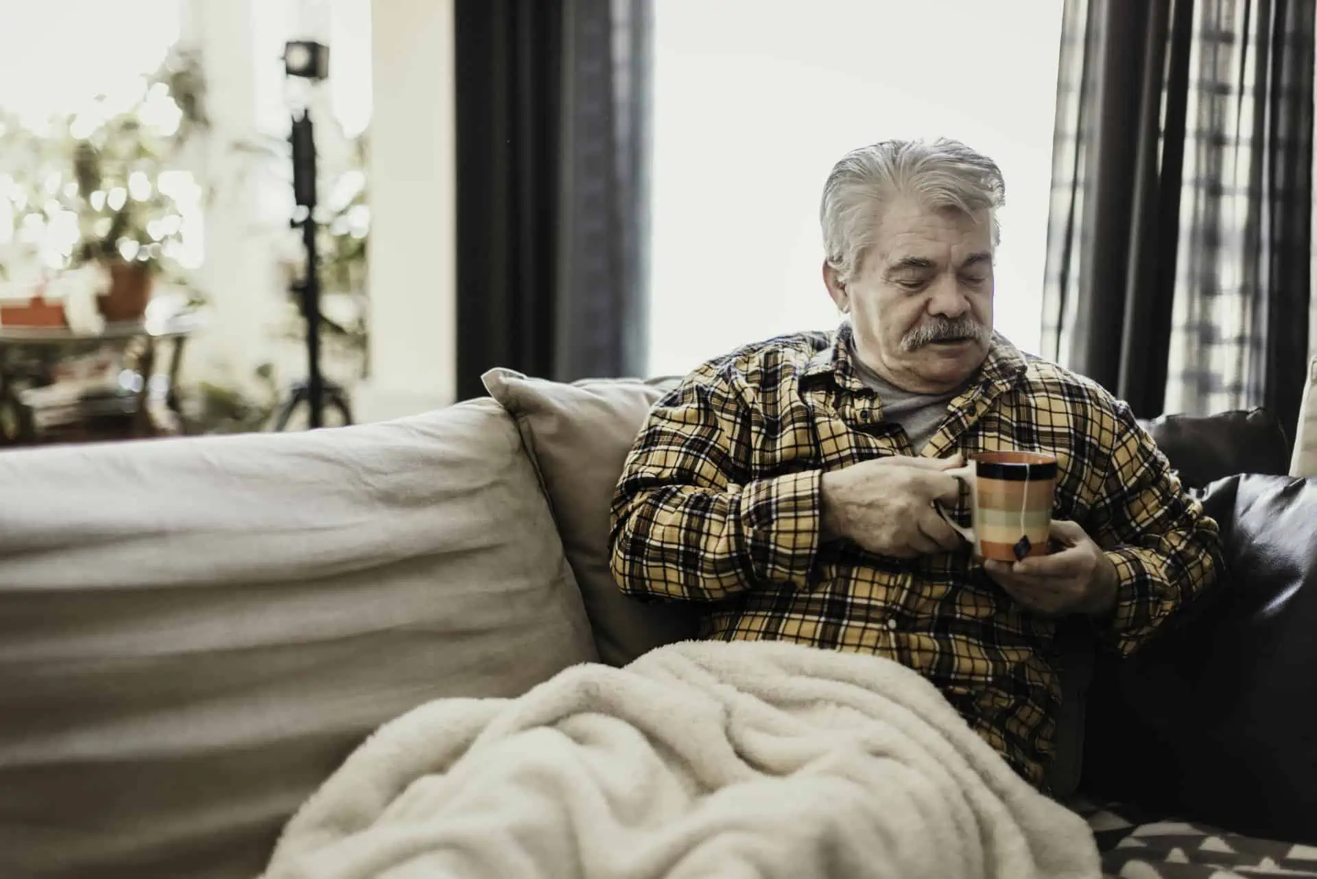 Senior man sitting on sofa wrapped in a warm blanket