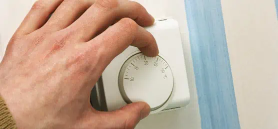 Close up of a person turning down a central heating thermostat
