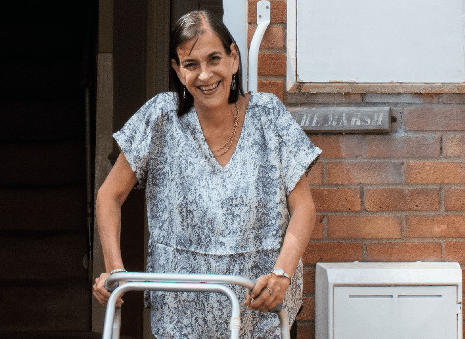 A woman using a walking frame in front of her home. Jayne is one of the many people supported by WHAM.