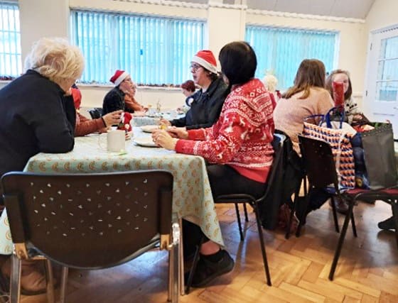 Visitors enjoying a cup of tea in a community centre. Some are wearing santa hats or christmas jumpers