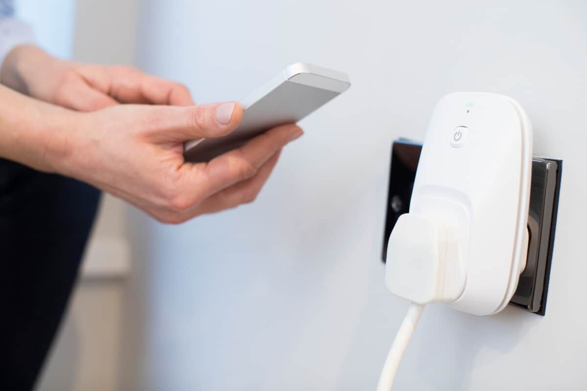 A close up of the hands of a woman controlling a smart plug using an app on her mobile phone