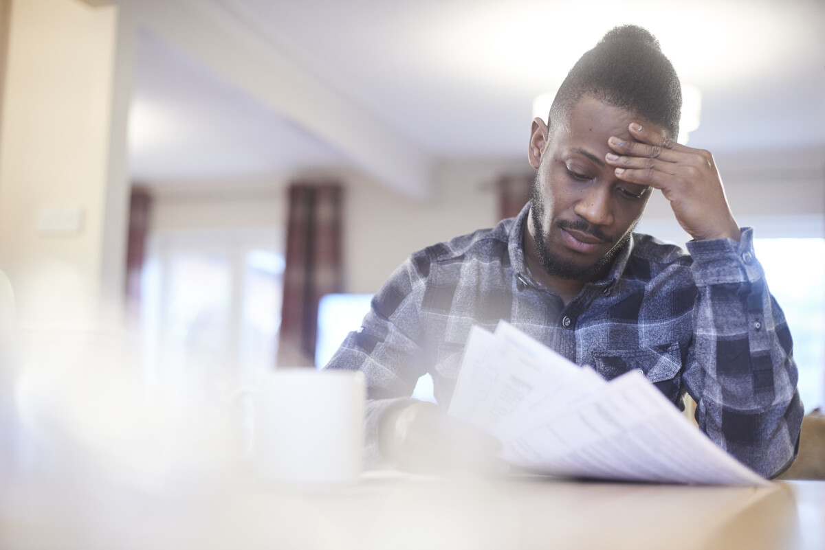 A man sits at a table reading a paper energy bill and looks worried.