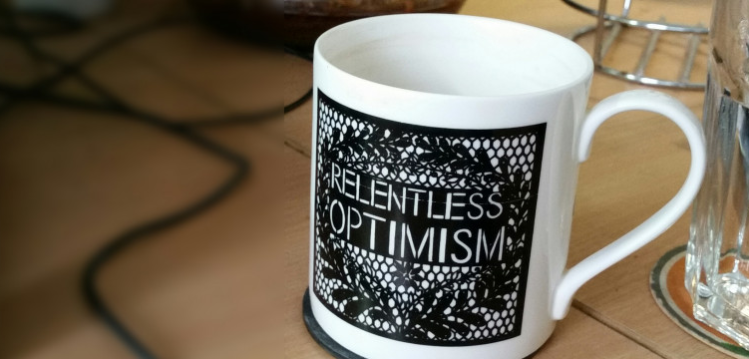 A coffee mug with the words 'Relentless optimism' written on it.