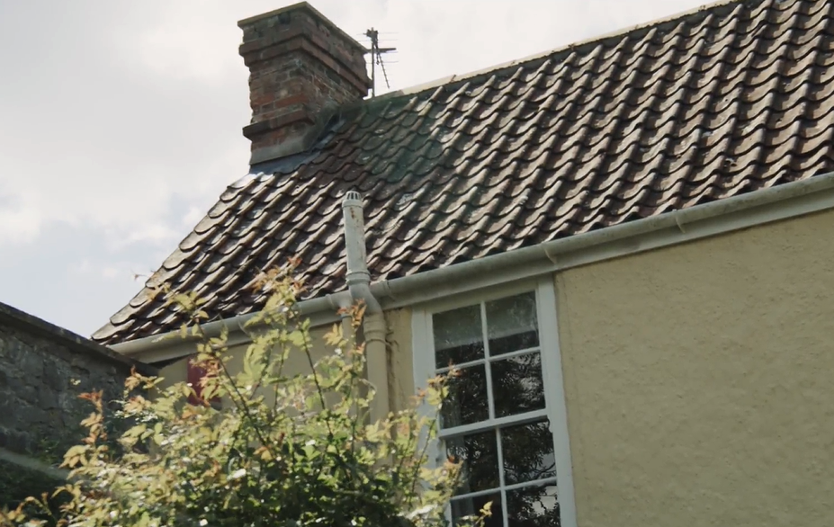 View of part of the outside of an old house showing the tiled roof and a traditional sash window.