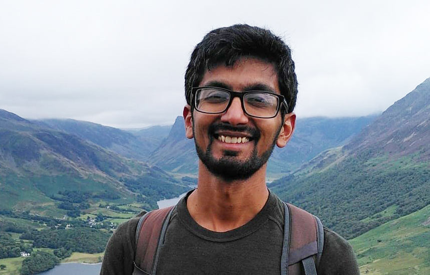 A headshot of a man smiling with hills in the background