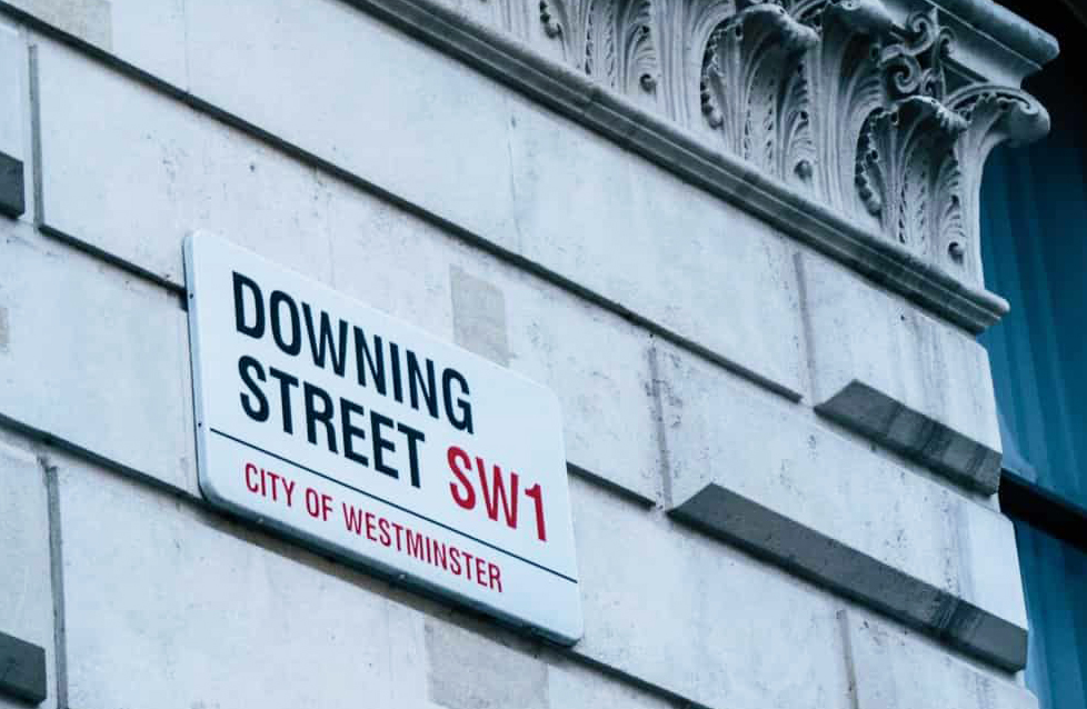 View looking up from street level at the Downing Street street sign attached to the wall of a grand building.