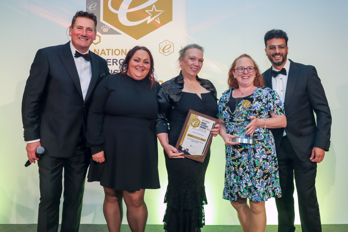 Five people pose smiling with a framed award