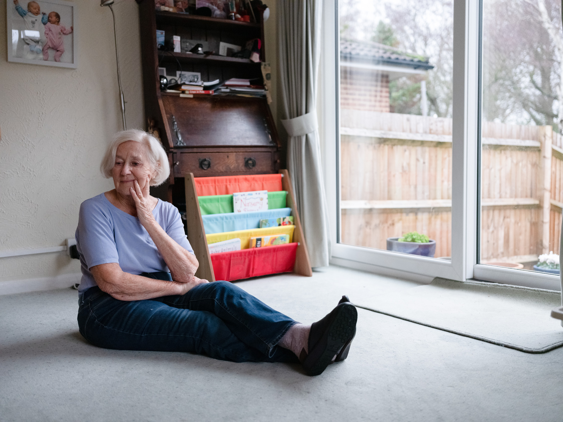 An older lady is sitting on the floor of her living room