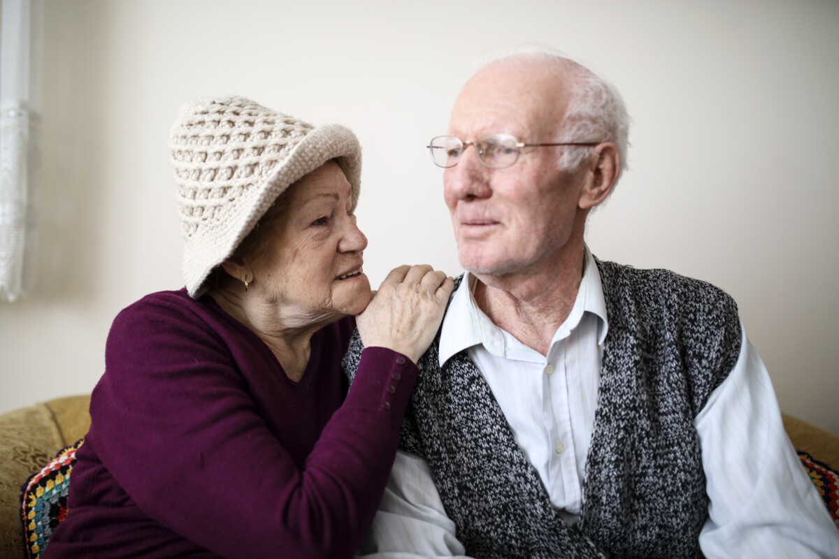 An elderly couple sit closely together on a sofa