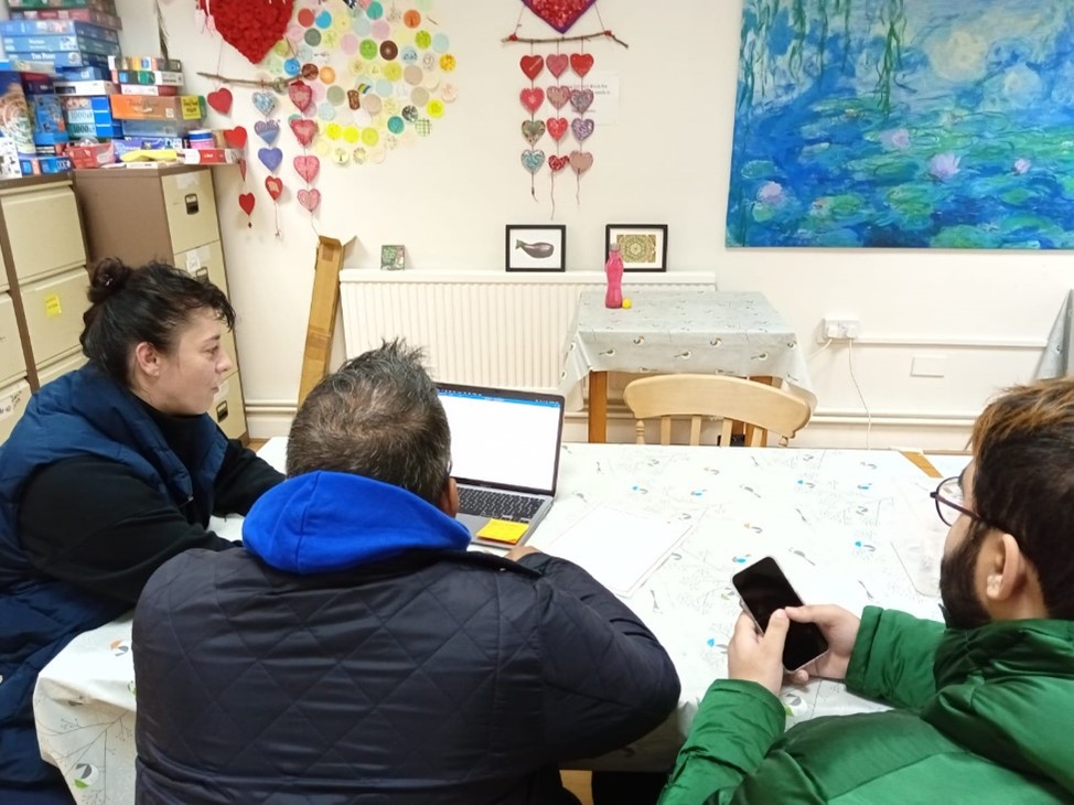 Three people sitting at a table looking at a laptop.