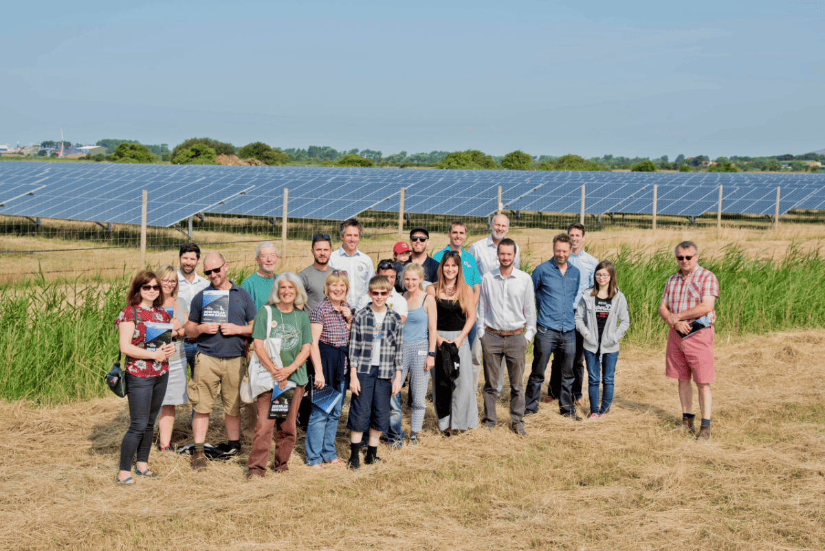A group of people pose for a photo in front of an array of solar panels in a field.