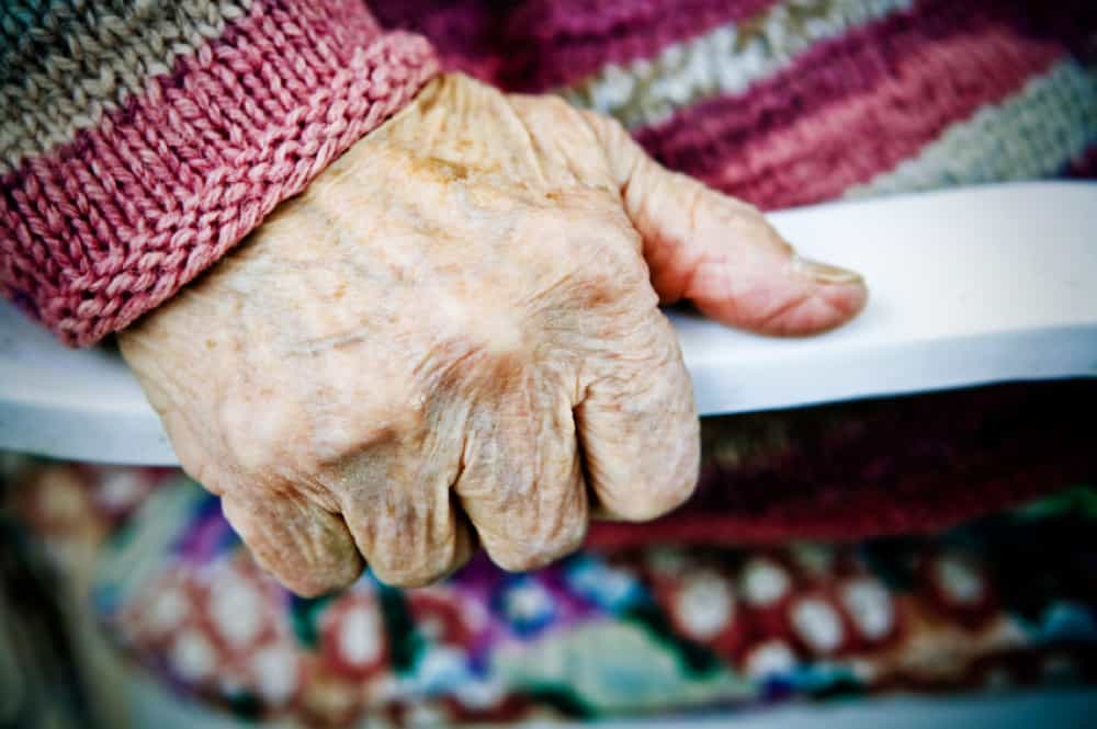 The hand of an older white person, gripping a chair's armrest.