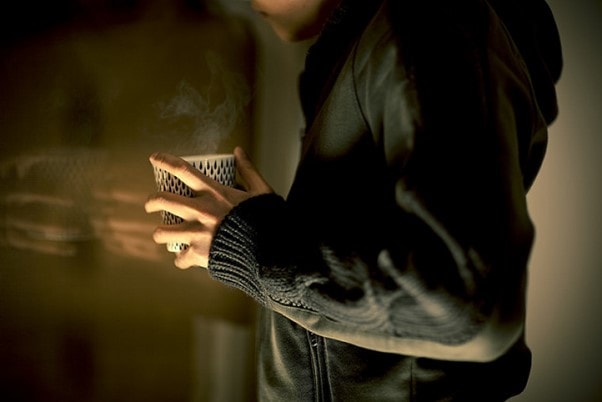 A photo of someone holding a steaming mug, cropped from shoulders to hips.