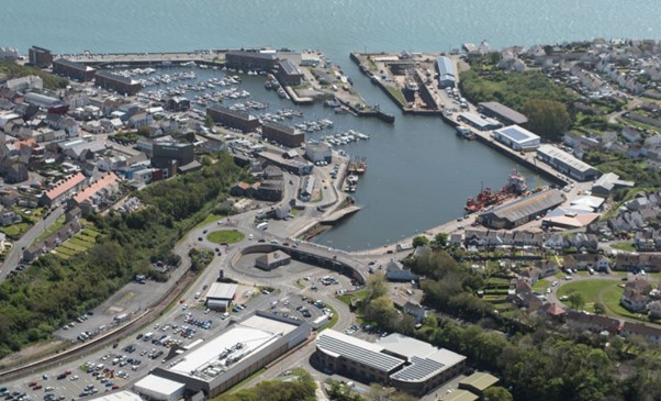 An aerial photograph of the port of Milford Haven. Buildings, roads and cars towards the bottom of the photo, the sea in the top half.