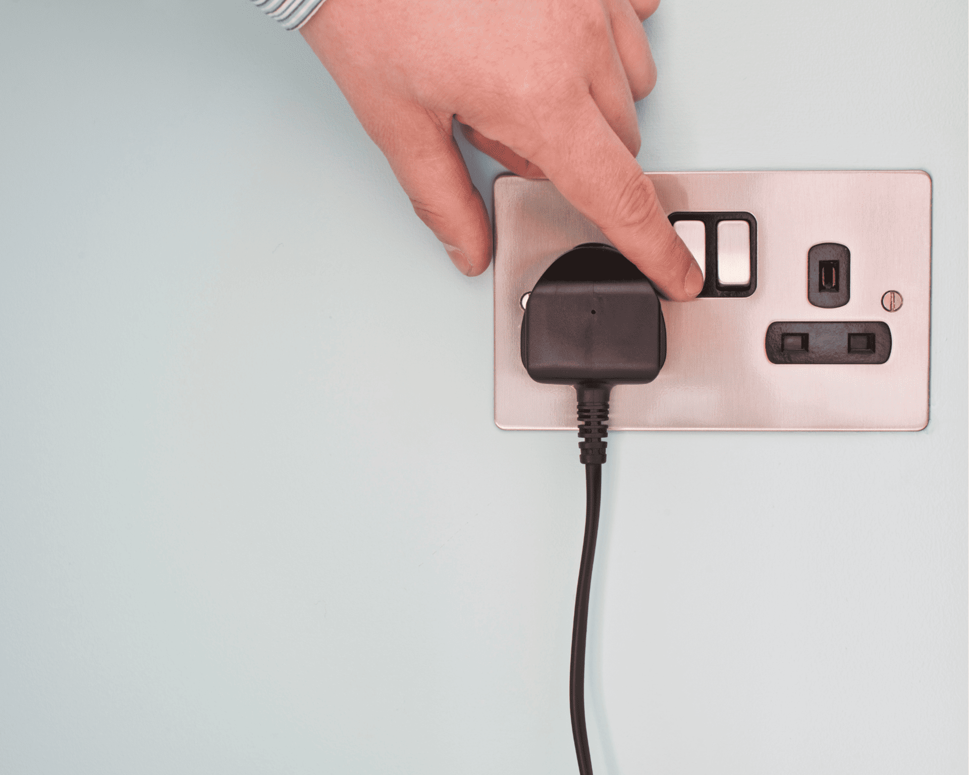 a hand with the finger over the switch of a plug socket. A black pug is connected to the left side socket with the cable hanging down.