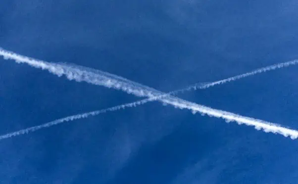 Two airplane trails create a white cross against a blue sky.