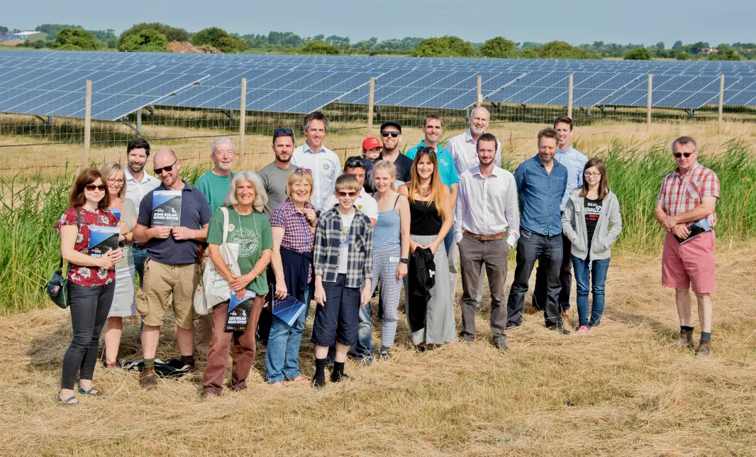 A group of people pose for a photo in front of an array of solar panels in a field.