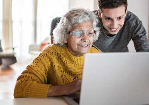 An elderly lady and her grandson look at the screen of an open laptop