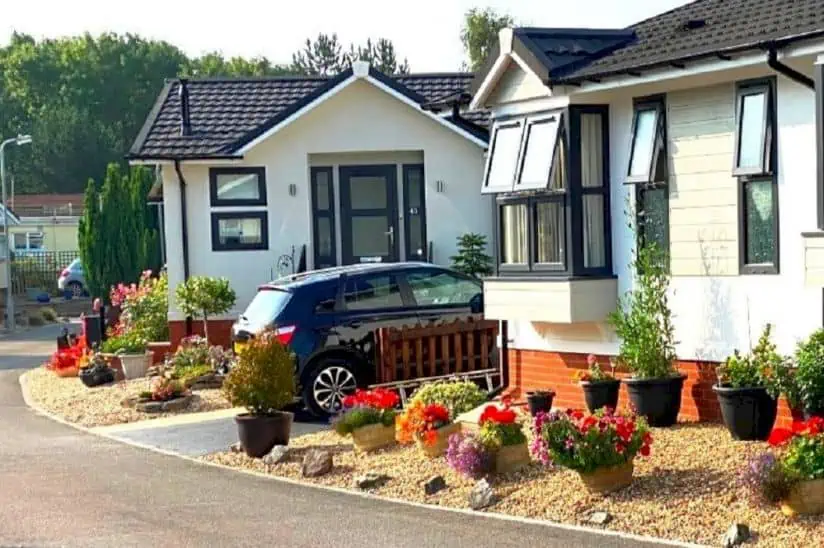 Two park homes surrounded by flowers in tubs. A car is parked on a drive between the two homes.