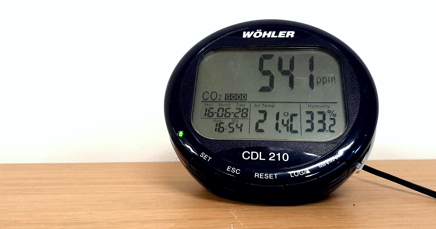 A black device with a screen showing a reading of 541 parts per million CO2, sitting on a wooden surface in front of a white wall.