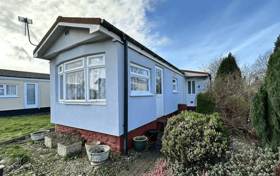 A park home painted blue with conifer trees around it.