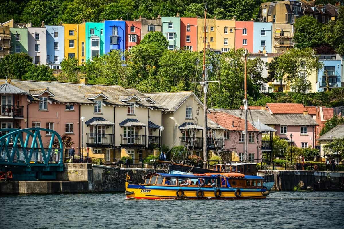 Ferry on a river, with a row of houses painted bright colours in the background.