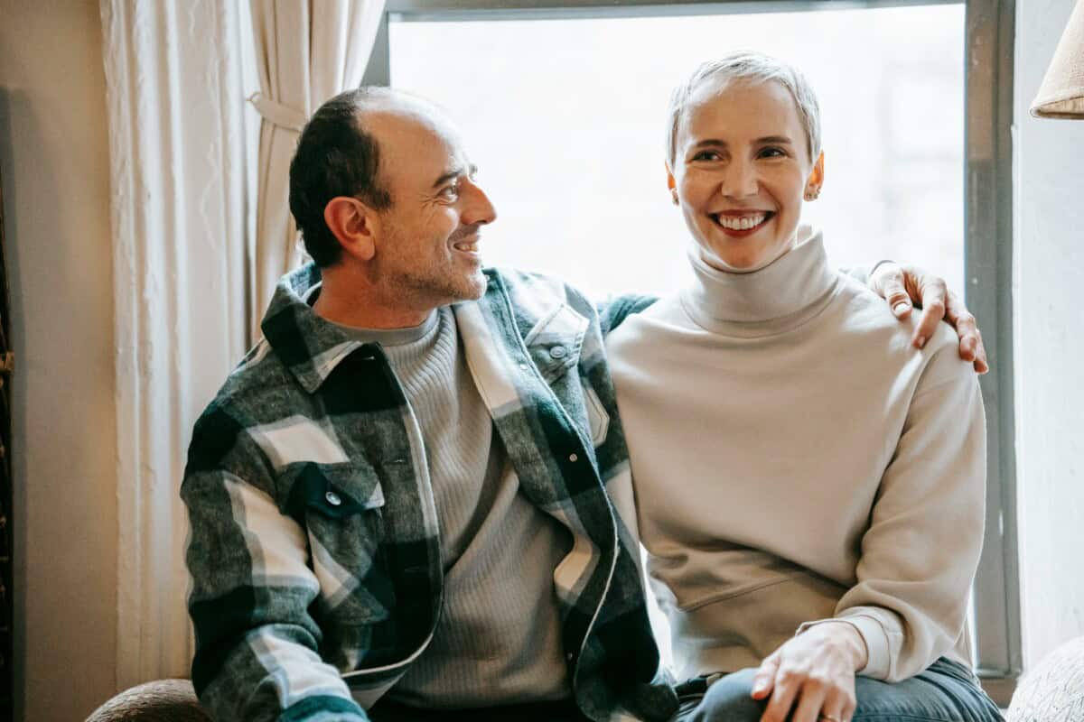 A similing man and woman sit by a window.