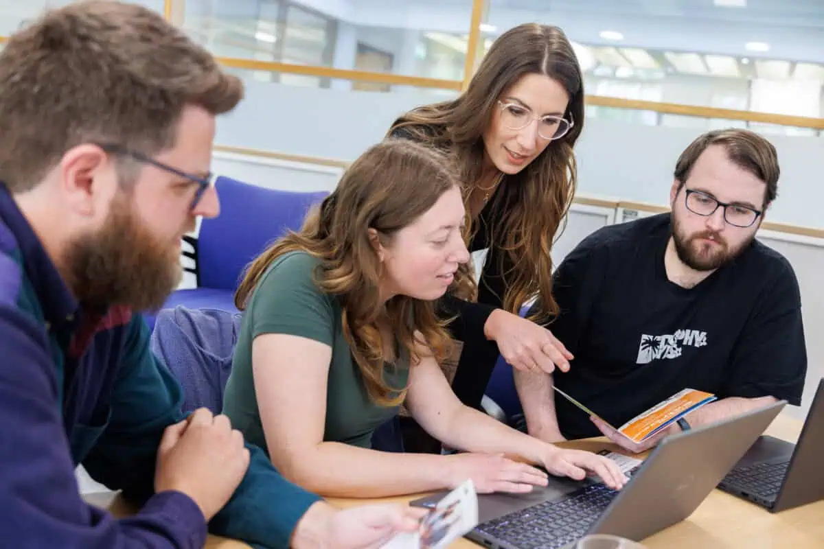 A group of four people gather round a computer screen. They are deep in discussion.