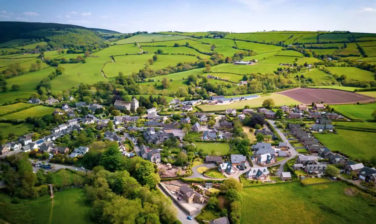 Aerial view of an English village surrounded by gentle hills, fields and woodland