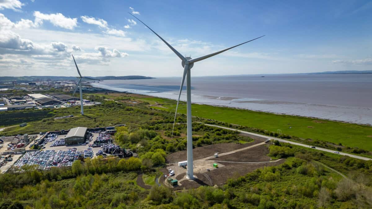 Drone-eye view of a large wind turbine in an industrial estate close to the coastline.
