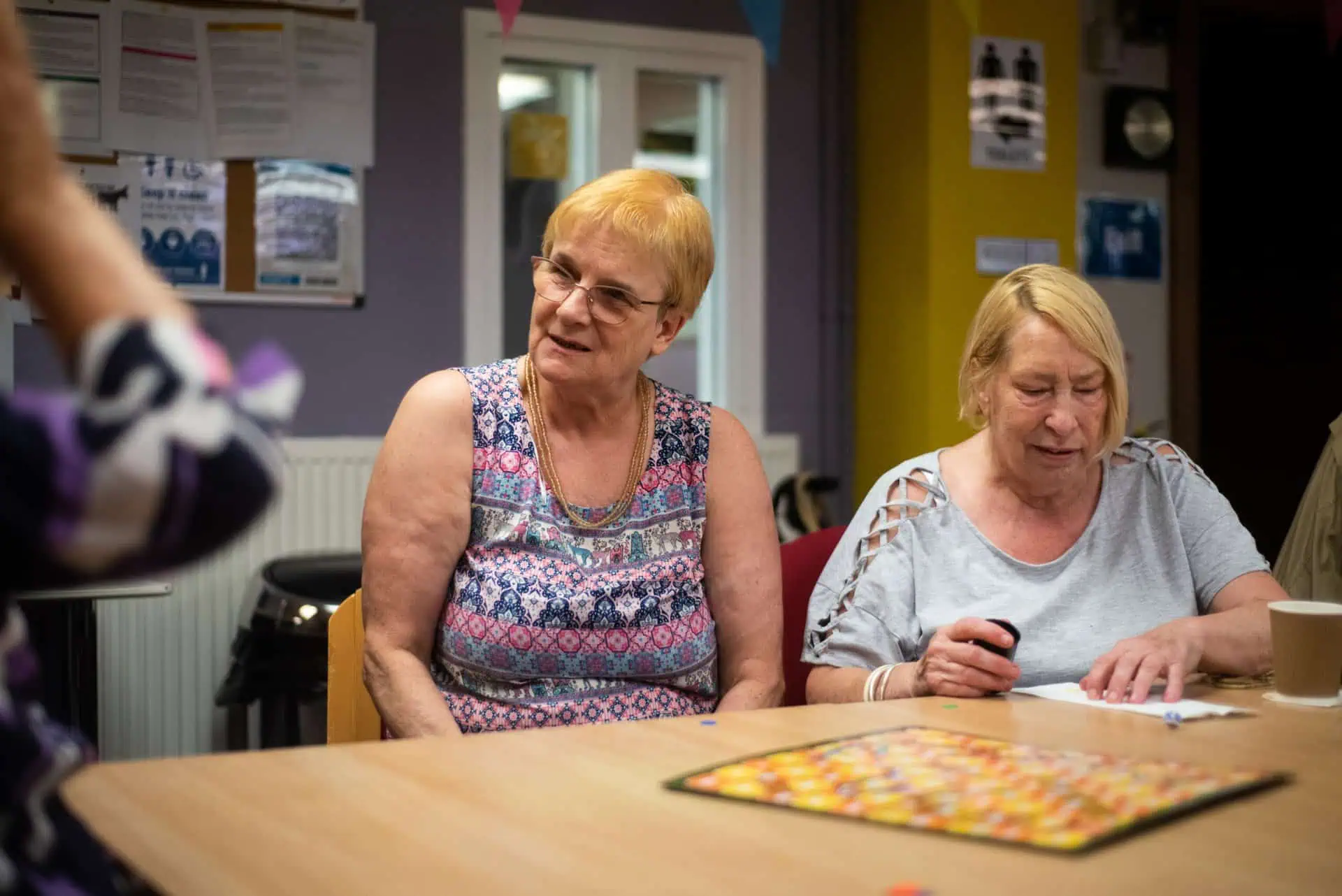Two women sit at a table smiling.