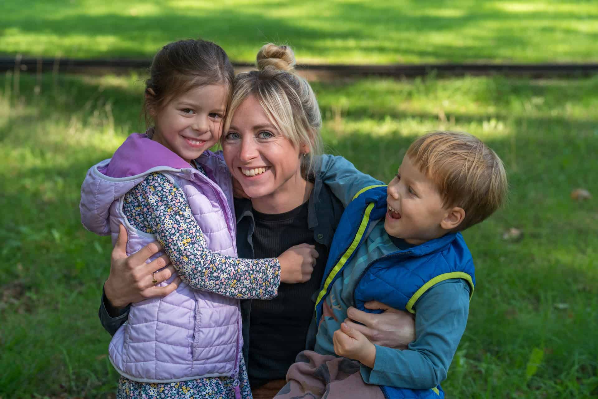 A young mother gently hugs her daughter and son on a walk.