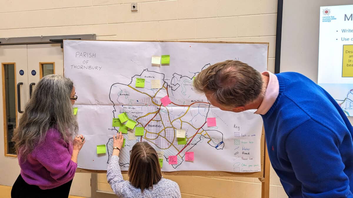Three adults stand in front of a whiteboard with a map. The child is adding a post-it.