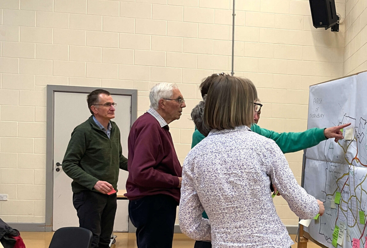 A group of four people stand in front of a white board placing post-it notes on a map.