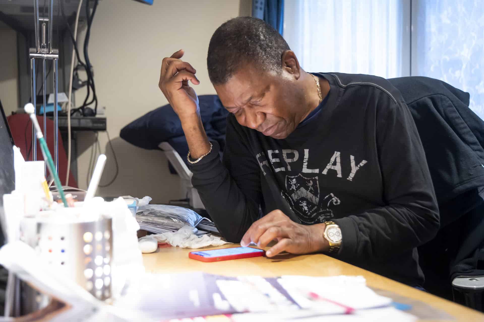A man sits at a desk looking at a smartphone.