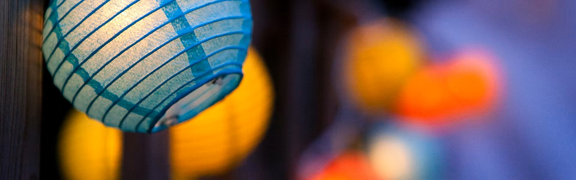 A teal lantern in focus with more yellow and orange lanterns blurred in the background
