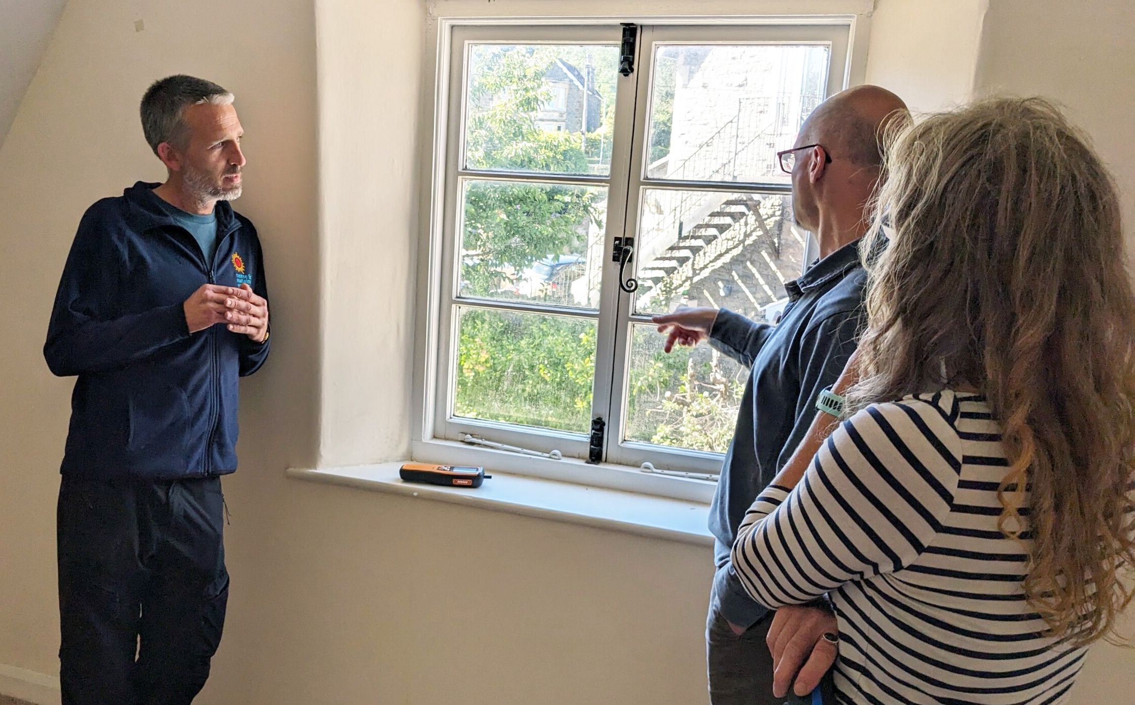 An energy advisor in branded fleece talks to home owners about a drafty window.