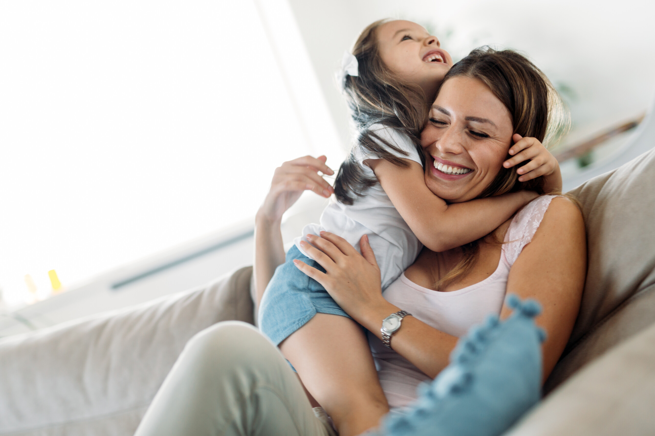 A mother and young daughter mucking about on a sofa looking happy.
